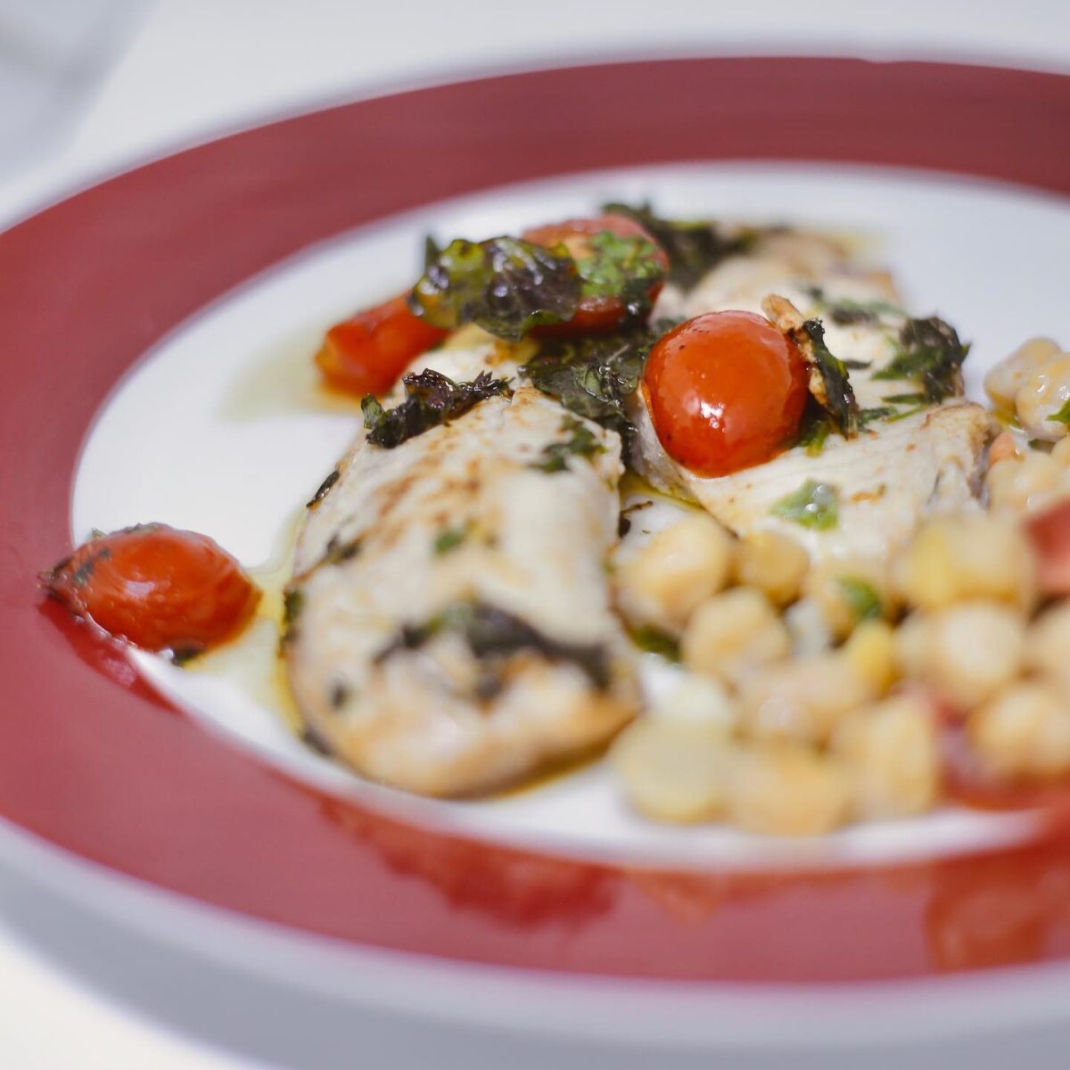 Frango grelhado com tomate cereja e grão de bico em prato vermelho